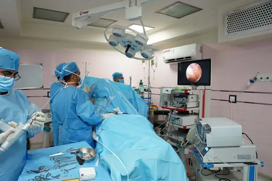 A surgical team at work in an operating room, with the endoscopic view on a wall-mounted screen