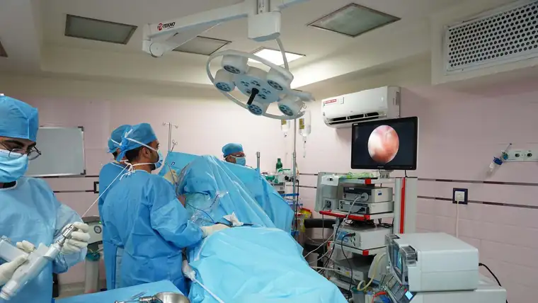 A surgical team at work in an operating room, with the endoscopic view on a wall-mounted screen